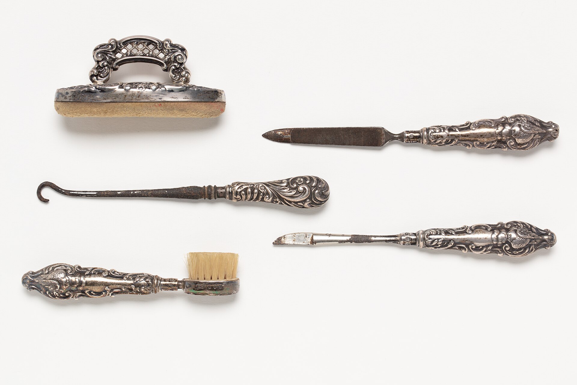 Juego de instrumentos de manicura de museo: tijeras, limas y empujadores de cutícula sobre fondo neutro.